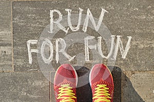 Run for fun, written on gray sidewalk with woman legs in sneakers, top view