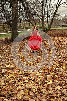 The runaway bride the girl in a red dress runs along the fallen autumn leaves before the storm