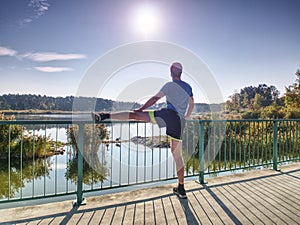 Runner in black leggings do body stretching on bridge path