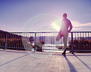 Runner in black leggings do body stretching on bridge path