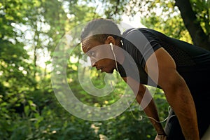 Runner in black t shirt leaning on knees, resting.