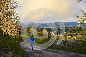 Runner in blue running in spring nature, with village in background. Sport active photo with copy space