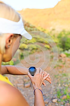 Runner checking sports watch in summer mountains on trail