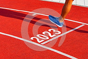 Runner crosses the finish line on a red treadmill with the numbers 2023. New year entry concept, step
