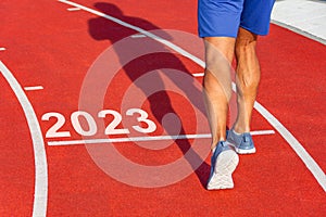 Runner crosses the line starting in 2023 on a red treadmill with the numbers 2023. New year entry concept, step