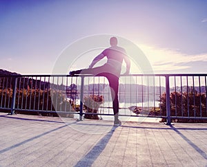 Runner doing stretching exercise on bridge. An active wiry man