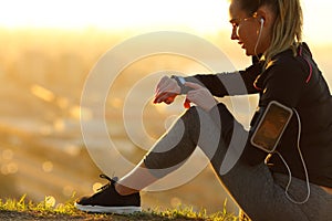 Runner with earphones checking smartwatch at sunset