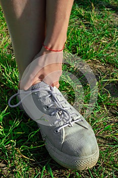 Runner girl outdoors on grass touching painful twisted ankle. Leg injury concept. Vertically