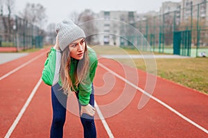 Runner having rest after training on winter sportsground on track. Woman working out outdoors. Sportive lifestyle