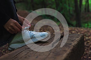 A runner or jogger woman tying her white sneaker in the forest