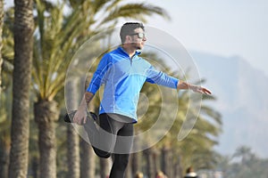 Runner man stretching at beach palm trees boulevard with sunglasses in morning jog training session