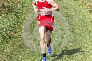 Runner running alone during a high school cross country 5K race on a grass field downhill