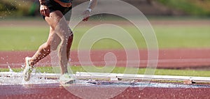 Runner running through the steeplechase water bake on a running track