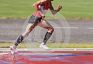 Runner running through the steeplechase water bake on a running track