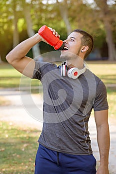 Runner smiling young latin man drinking water running portrait format sports training fitness workout
