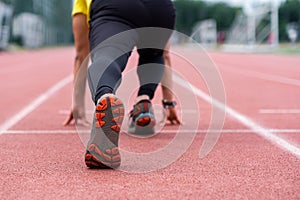 Runner standing in low start position ready to run along red rubberized track on ground