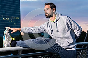 Runner stretching in front of office building at sunset