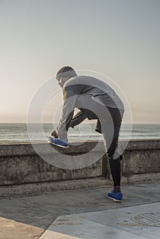 Runner ties shoe by wall near ocean