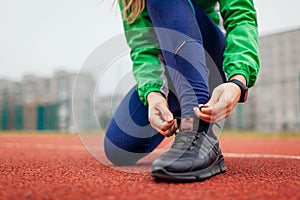 Runner tying shoe laces on running track. Woman training on autumn sportsground. Active healthy sportive lifestyle