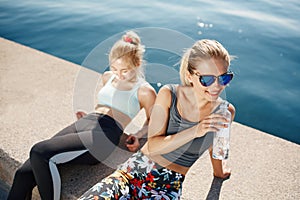 Runner woman drinking water on beach with asian friend running