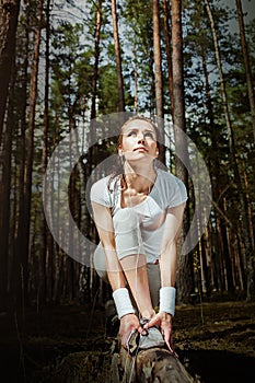 Runner woman stretching thigh before running in forest and looking to the sky.