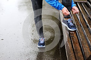 Runner woman tying laces before training in the rain. Marathon.
