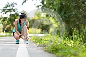 Runner young asia woman tying laces of running shoes before jogging through the road in the workout nature park.