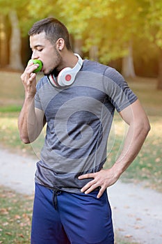 Runner young latin man eating apple portrait format running jogging sports training fitness