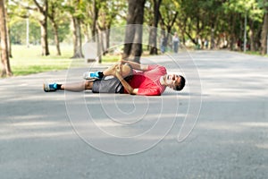 Runners catch knee from accident in public park. Injury from run. Man wearing red shirt lying on the road inside the Park