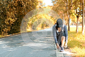 Running asian woman tying laces of running shoes before jogging through the road in the workout nature autumn park.