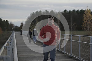 Running in cold fall weather in nature. A man runs across wooden bridge in national park. An athlete in cross country