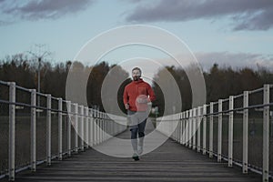 Running in cold fall weather in nature. A man runs across wooden bridge in national park. An athlete in cross country