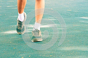 Running feet male in runner jogging exercise with old shoes for health lose weight concept on track rubber cover blue public park