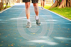 Running feet male in runner jogging exercise with old shoes for health lose weight concept on track rubber cover blue public park