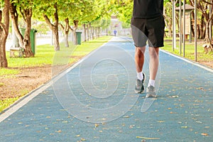 Running feet male in runner jogging exercise with old shoes for health lose weight concept on track rubber cover blue public park