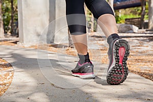 Running feet of young woman going by concrete trail in the park