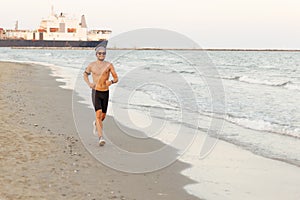 Runner training outside working at the beach. Fit young male sport fitness model exercising in full body in summer