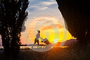 Running mother with stroller enjoying motherhood at sunset lands