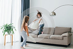 Running with pillows. Kids having fun in the domestic room at daytime together