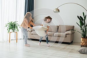 Running with pillows. Kids having fun in the domestic room at daytime together