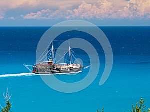 Running pirate corsair style boat ship in amazing Greece island bay with swimming people, beach in Ionian Sea blue water, Famous G