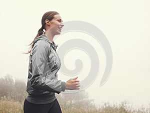 Running puts a smile on her face. A young woman jogging on a country road on a misty morning.