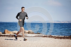 Running on the sand is a great workout. Shot of a handsome young man running on the beach.