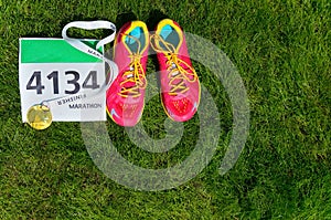 Running shoes, marathon race bib (number) and finisher medal on grass background,