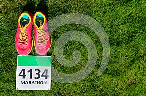 Running shoes and marathon race bib (number) on grass background, sport, fitness and healthy lifestyle