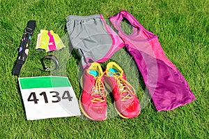 Running shoes, marathon race bib number, runner gear and energy gels on grass background, sport competition