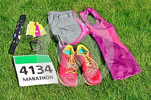 Running shoes, marathon race bib number, runner gear and energy gels on grass background, sport competition, fitness