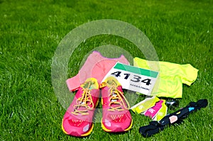 Running shoes, marathon race bib number, runner gear and energy gels on grass background, sport competition photo