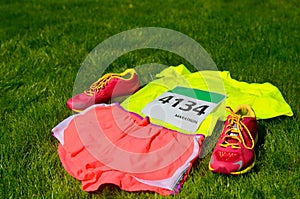 Running shoes, marathon race bib (number), runners gear and energy gels on grass background