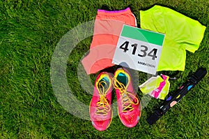 Running shoes, marathon race bib (number), runners gear and energy gels on grass background
